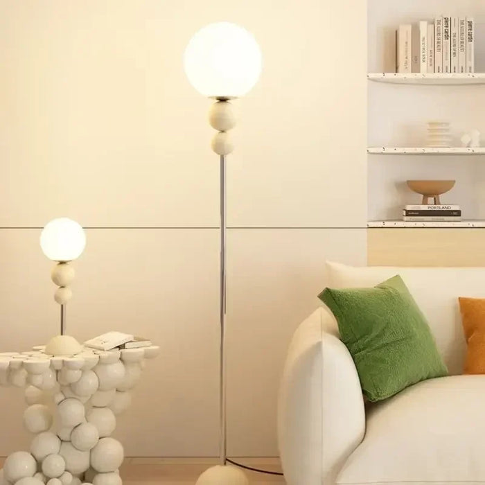 Cremefarbene Stehleuchte mit Glaskugel neben einem hellen Sofa
