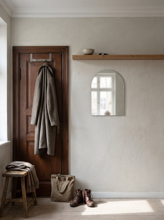 Rahmenloser Bogen-Wandspiegel an einer Flurwand unter einem Holzbord im Morgenlicht