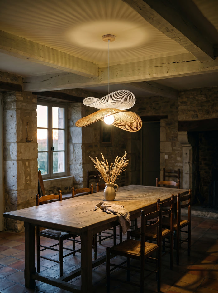 Rattan-Pendelleuchte mit cremeweißer und naturfarbener Lage über einem langen Holztisch in einem Steinhaus