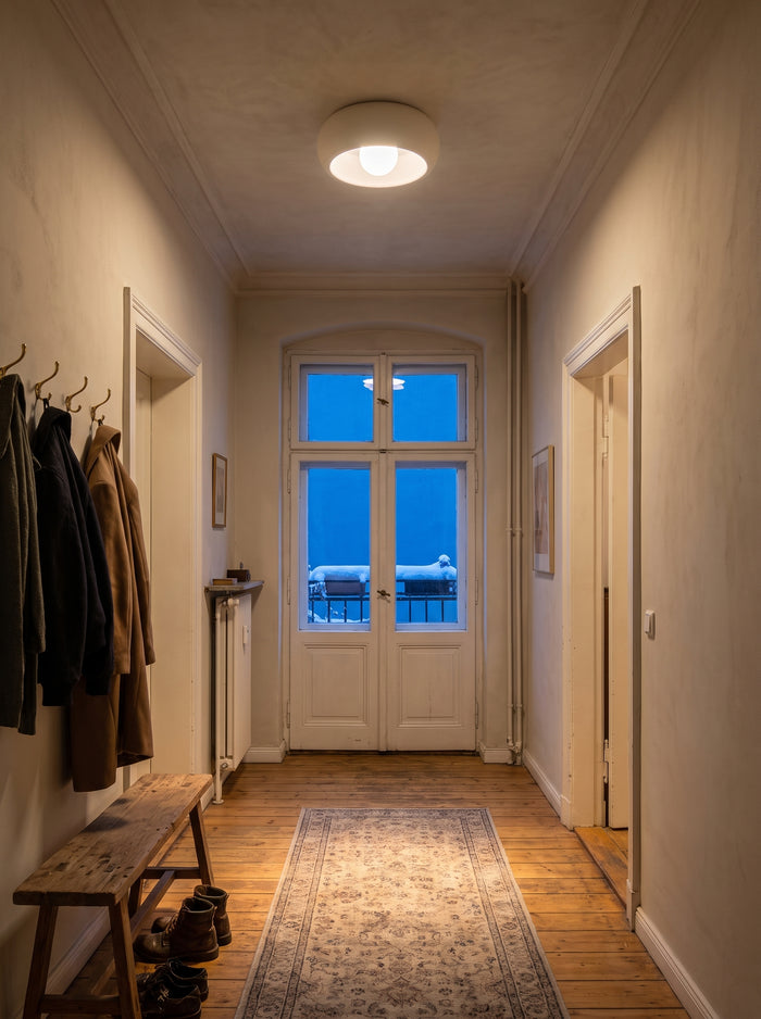 Runde mattweiße Deckenleuchte im Altbauflur mit Dielen, Garderobe und Balkontür zur verschneiten Terrasse