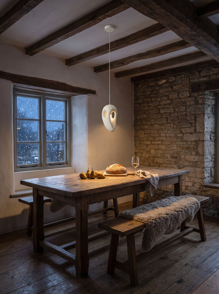 Weiße Pendelleuchte aus Kunstharz über einem rustikalen Holztisch in einem Steinhaus mit Holzbalken