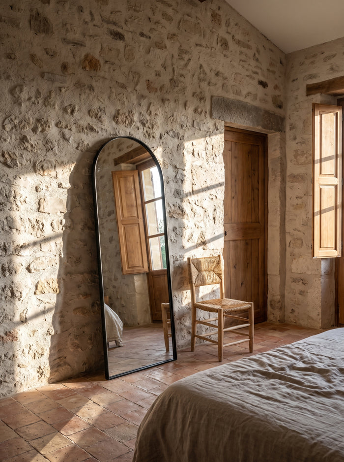 Bogenspiegel 150 × 50 cm mit schwarzem Rahmen an einer Bruchsteinwand im Schlafzimmer, Nachmittagssonne auf Terrakottaboden