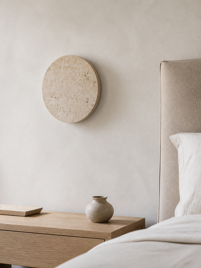 Runde Wandleuchte aus hellem Travertin neben einem Bett bei Tageslicht